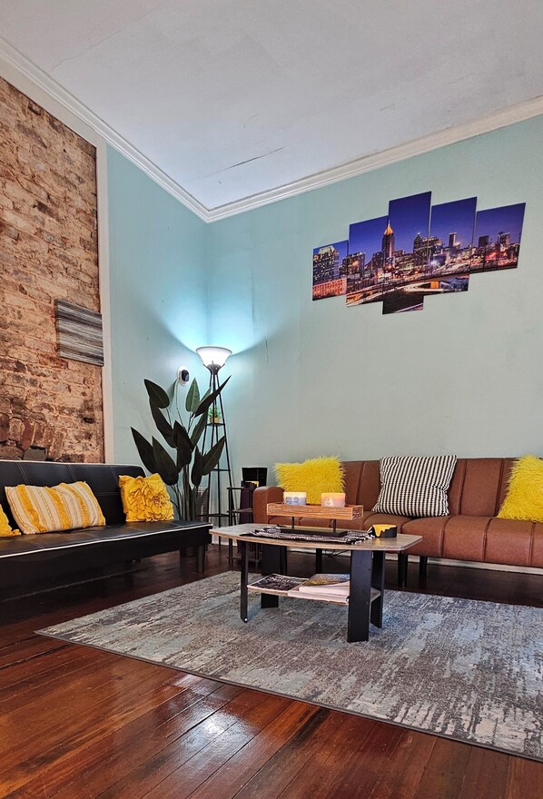 A living room with a black sofa, a brown sofa, a coffee table, a floor lamp, and a cityscape wall art. - Charming Historic Cabbagetown Home / Atlanta Gem! Close to Atlanta Stadium FIFA! (Atlanta)