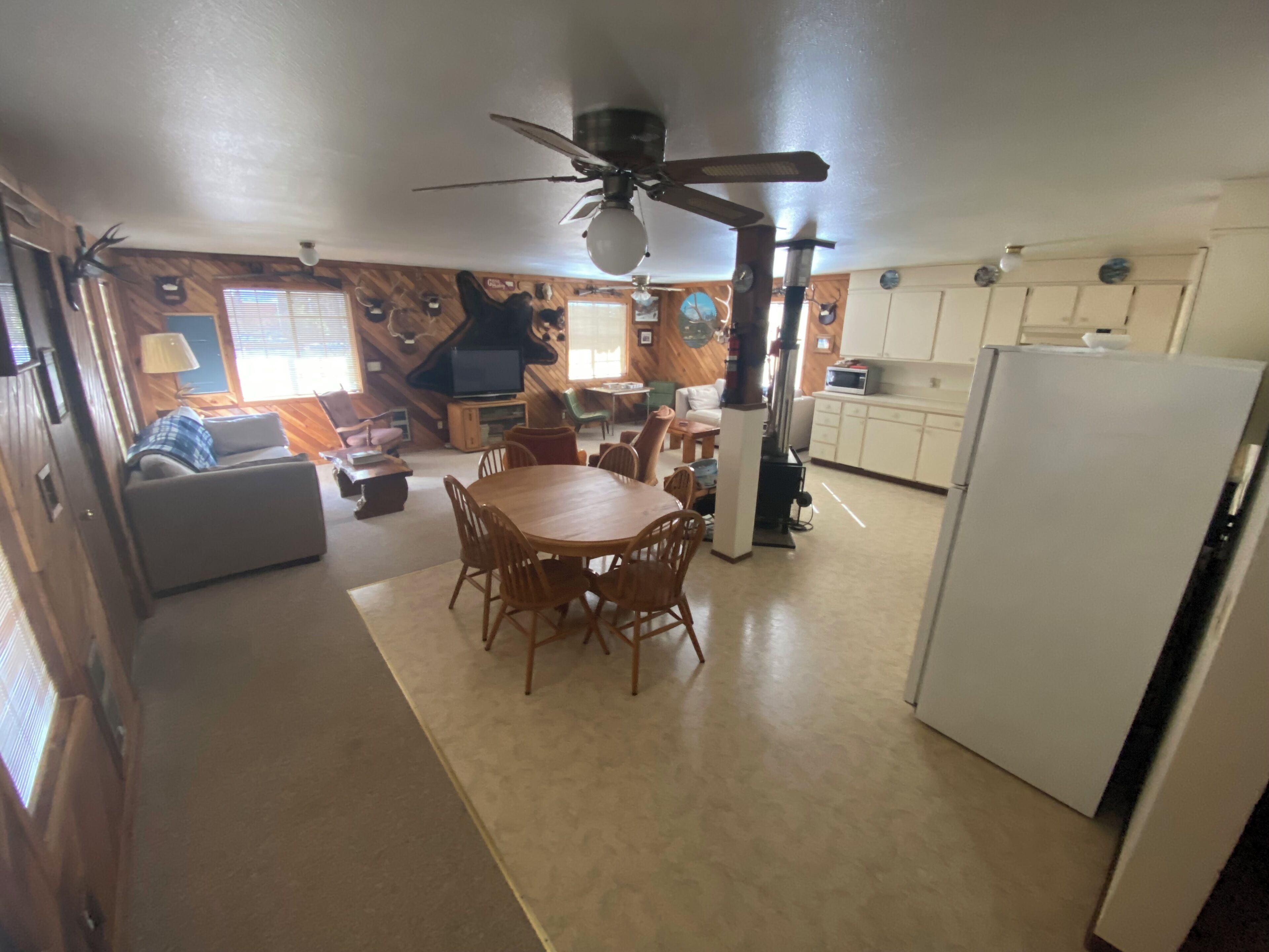 A spacious kitchen with a dining area, wooden walls, and a ceiling fan.