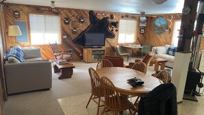 A cozy living room with a fireplace, wooden walls, a television, and a dining area with chairs and a table. - Rustic Retreat in Charming Leavenworth- Wifi and W/D! (Leavenworth)