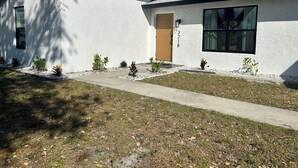 Une maison moderne à deux étages, avec une façade blanche, un chemin en béton et de petites plantes dans le jardin.