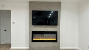 Un salon moderne avec un téléviseur à écran plat fixé au-dessus d’une cheminée.