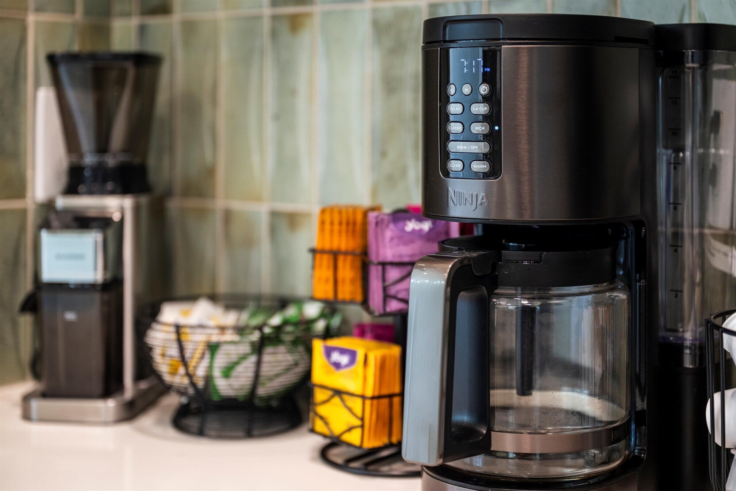 Une machine à café dotée d’une interface numérique, une balance et un panier de dosettes de café, le tout posé sur un plan de travail de cuisine.