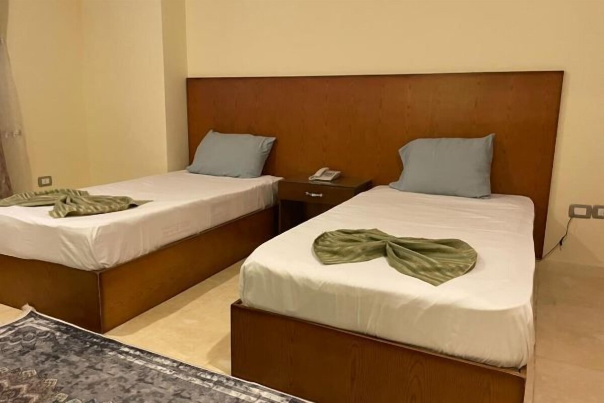 A hotel room with two single beds, each with a wooden headboard and a bedside table.