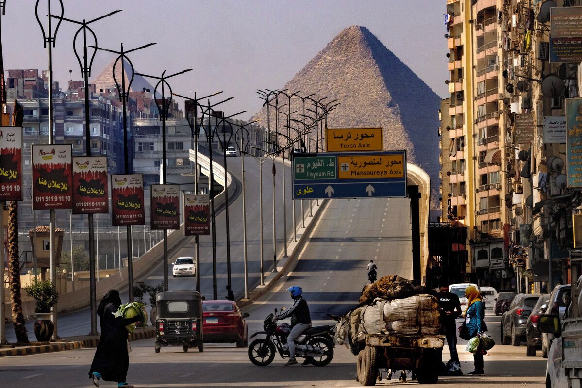 Eine Straße mit einer Pyramide im Hintergrund, Verkehrsschildern sowie Autos und Fußgängern.