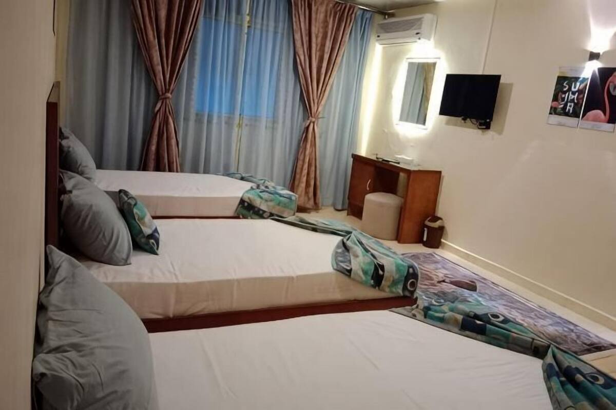 A hotel room with two beds, a desk, a chair, a TV, and curtains.