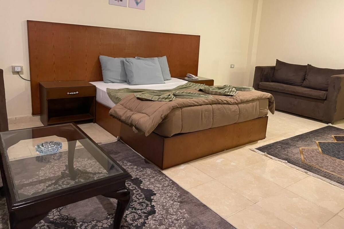 A hotel room with a bed, a sofa, a glass coffee table, and a nightstand.