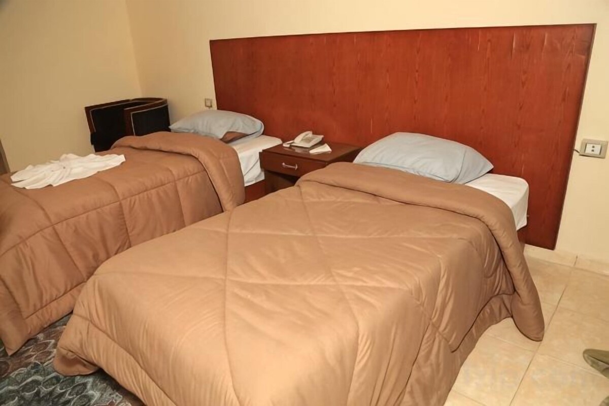 A hotel room with two beds, a wooden headboard, a nightstand, and a telephone.