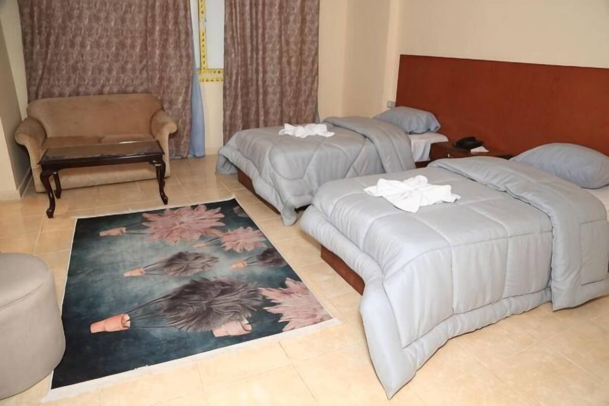 A hotel room with two beds, a sofa, a coffee table, and a floral rug.