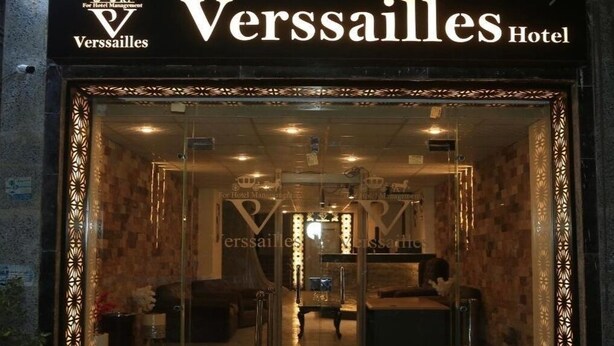 L'ingresso dell'Hotel Verssailles, con facciata in vetro, una reception e una zona salotto visibili all'interno.