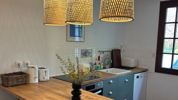 A modern kitchen with a wooden island, three hanging pendant lights, a toaster, a kettle, and a sink. - House of Peace and Nature (Charencey)