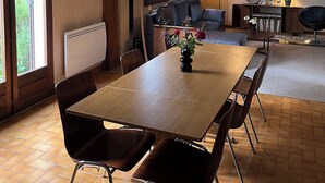 A dining area with a wooden table and chairs, a chandelier, and a view of the outdoors through a large window. - House of Peace and Nature (Charencey)