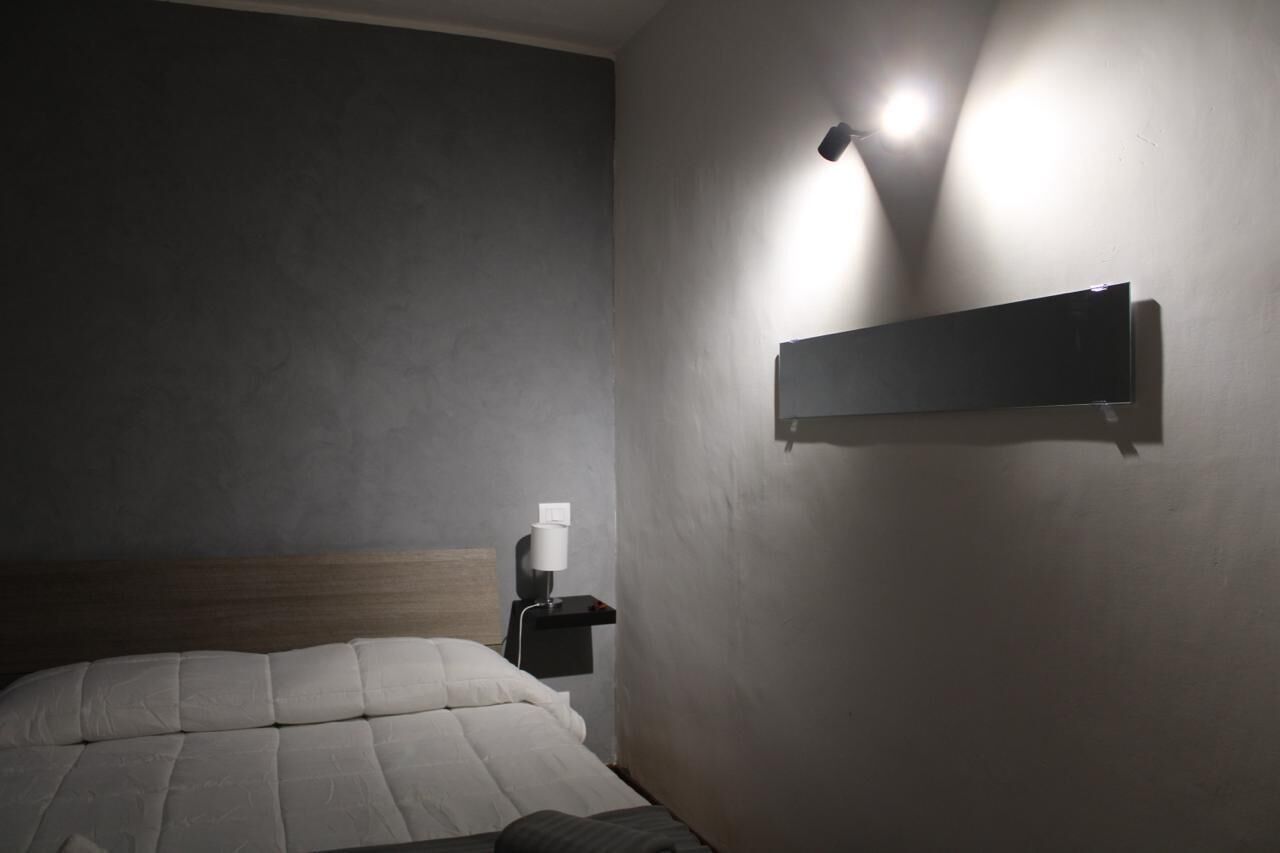 Une chambre d’hôtel avec un lit, une table de chevet avec une lampe et une étagère fixée au mur.