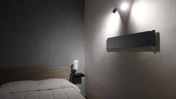 Une chambre d’hôtel avec un lit, une table de chevet avec une lampe et une étagère fixée au mur.