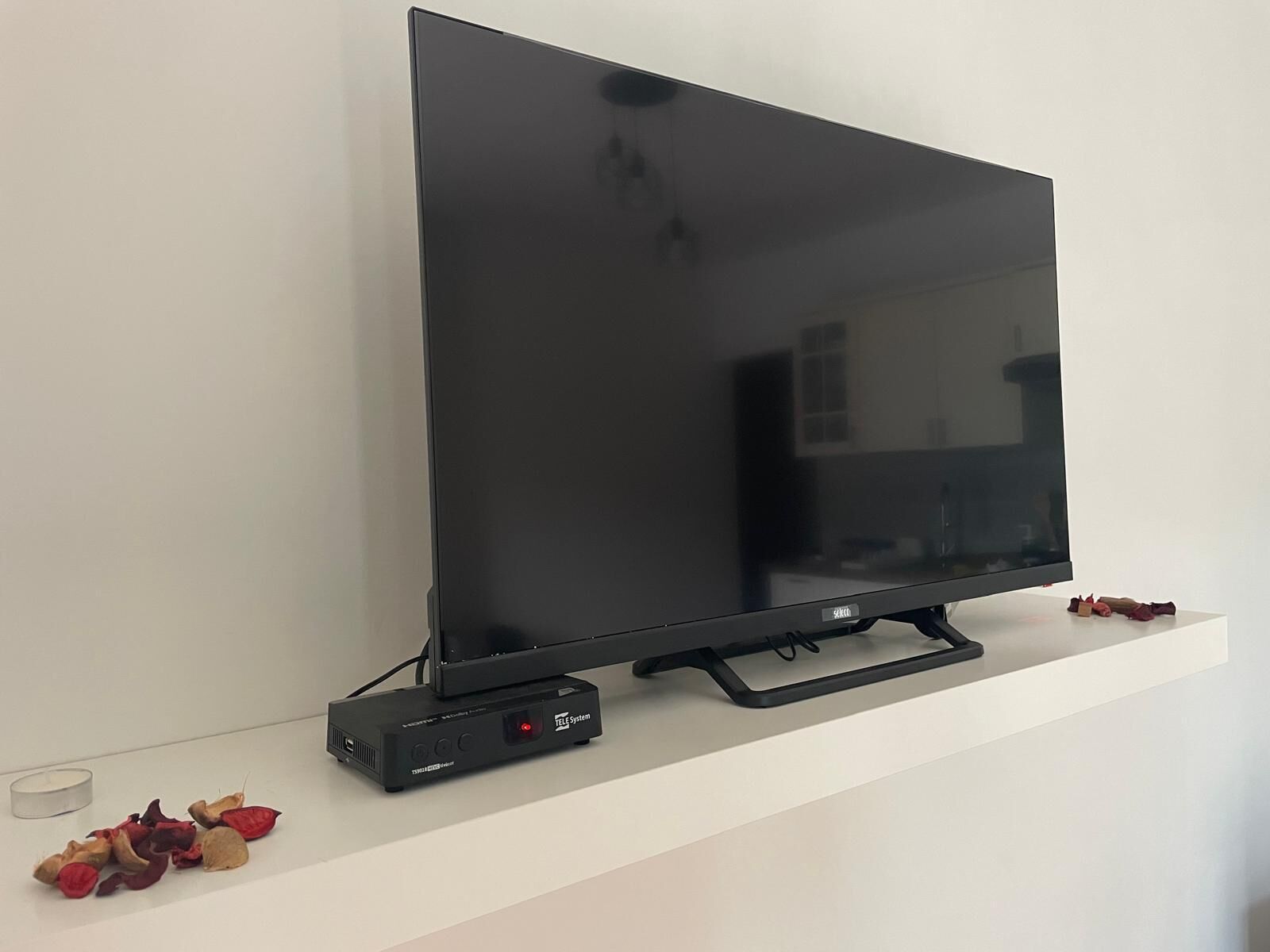 A flat-screen TV on a white shelf with a TELE System device below it.