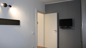 Une pièce avec une porte fermée, un téléviseur fixé au mur et un luminaire fixé au mur.