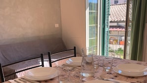 Une table à manger dressée avec des assiettes, des verres et des couverts, recouverte d’une nappe ornée d’un motif d’époque.