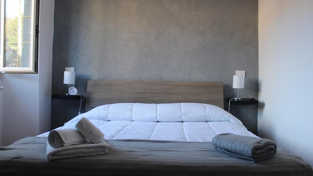 Un lit bien fait, avec une tête de lit en bois, deux tables de chevet avec des lampes et une fenêtre sur le côté gauche.