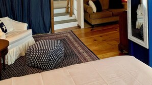 Ett sovrum på entresolplan med högt tak, synliga träbjälkar, en säng, en soffa och en trappa som leder upp till en övre våning.