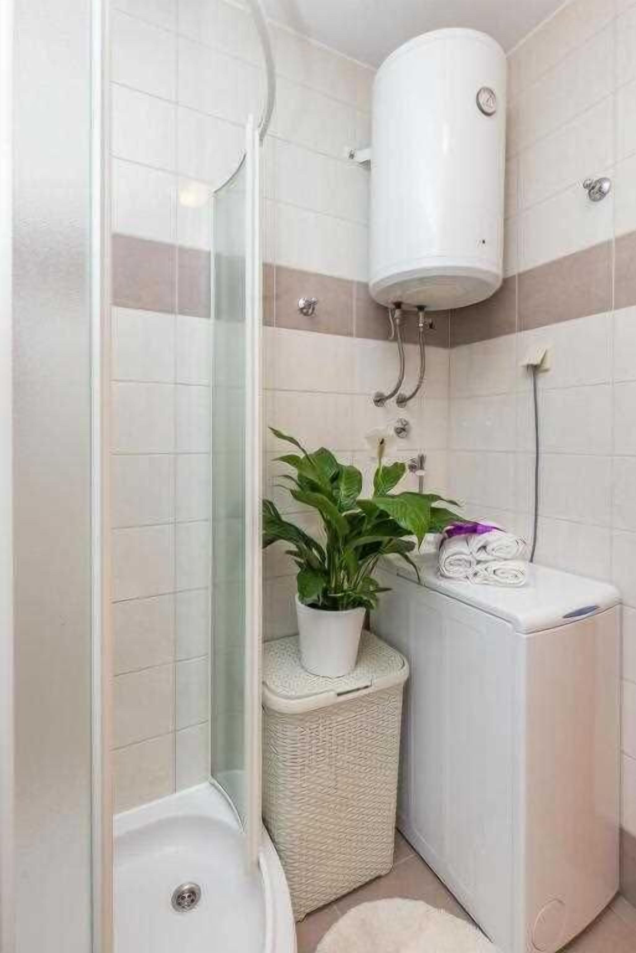 Une salle de bain moderne avec une douche à parois de verre, des toilettes blanches, un lavabo blanc et une plante en pot.