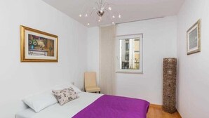 A bedroom with a bed, a chair, a window, and a painting on the wall.