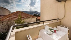 A balcony with a table set for two, overlooking a residential area with red-tiled roofs and a mountain in the distance.