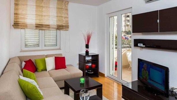 A living room with a beige sofa, a small coffee table, a TV, and a sliding glass door leading to an outdoor area.