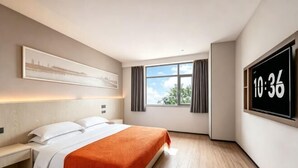 Ένα δωμάτιο ξενοδοχείου με ένα κρεβάτι, ένα κομοδίνο, ένα μεγάλο παράθυρο με κουρτίνες, μια τηλεόραση τοποθετημένη στον τοίχο που δείχνει την ώρα και έναν πίνακα με κορνίζα πάνω από το κρεβάτι.
