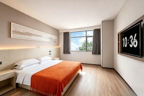 A hotel room with a bed, a nightstand, a large window with curtains, a wall-mounted TV displaying the time, and a framed picture above the bed.