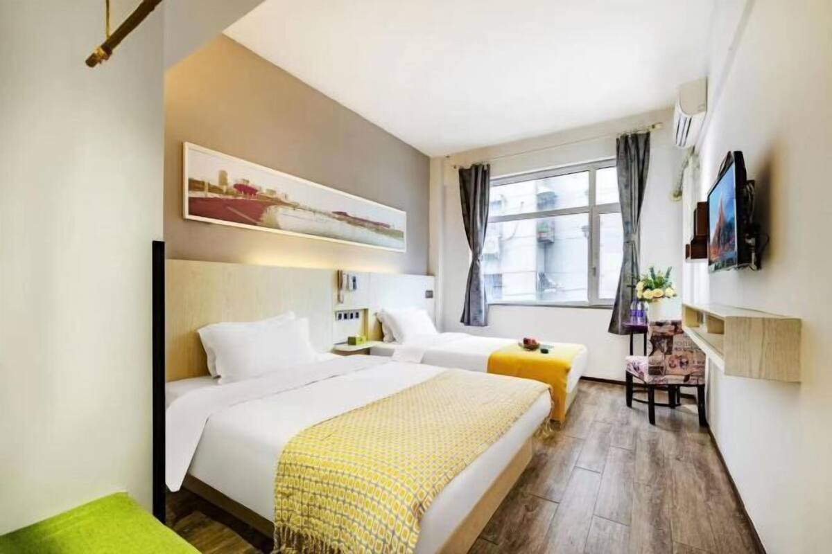 Une chambre d’hôtel avec deux lits, un bureau, une chaise, une télévision et une fenêtre avec des rideaux.