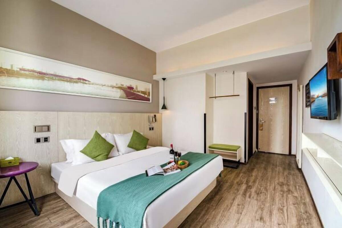 Une chambre d’hôtel avec un lit, une petite table, un banc, un téléviseur et une porte donnant sur une autre pièce.