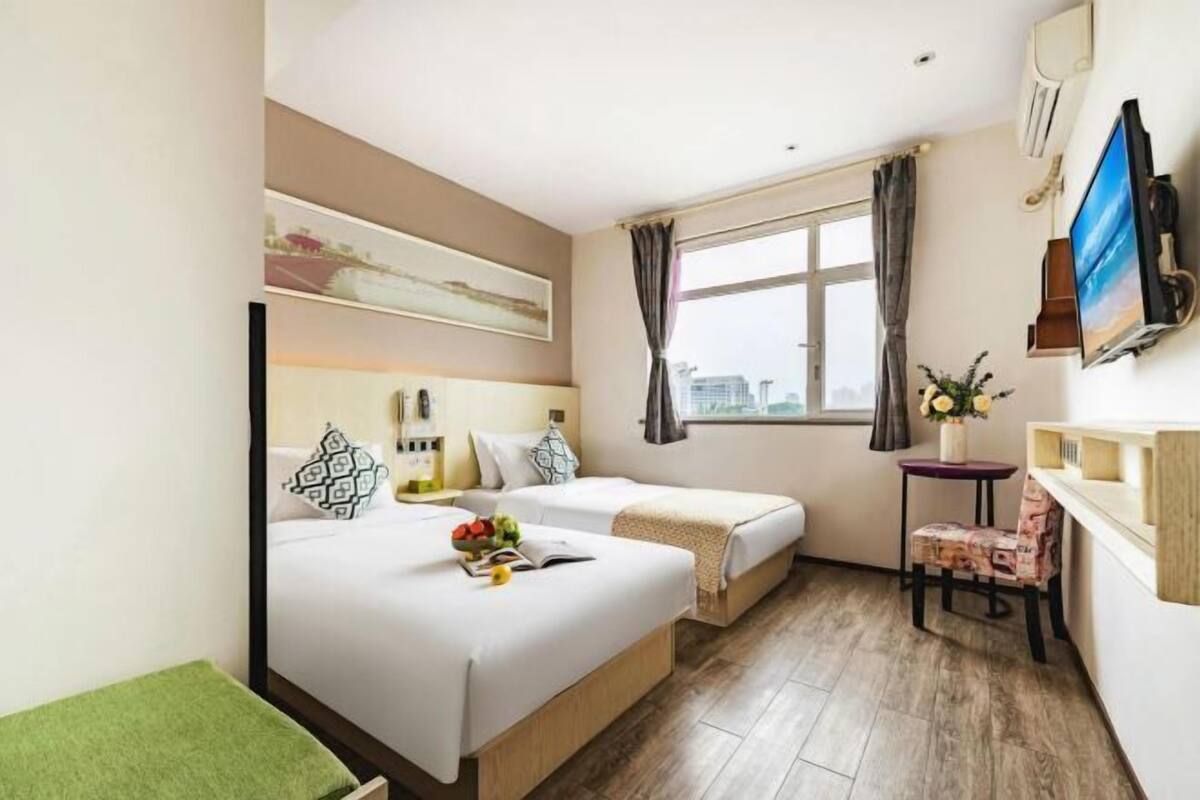 Une chambre d’hôtel avec deux lits, une petite table avec une chaise, une télévision et une fenêtre avec des rideaux.