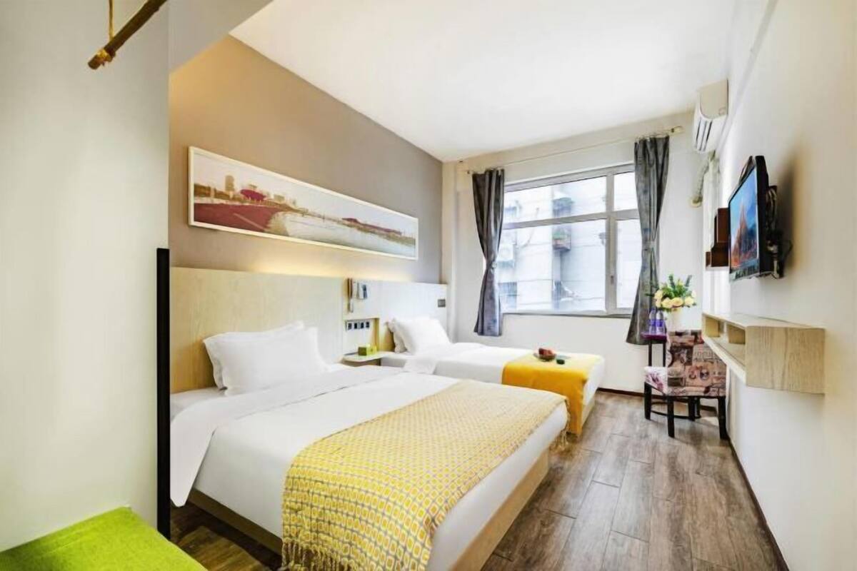 Une chambre d’hôtel avec deux lits, un bureau, une chaise, une télévision et une fenêtre avec des rideaux.
