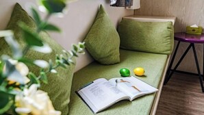 Ένας πράσινος καναπές με μαξιλάρια, ένα βιβλίο και δύο λεμόνια πάνω του.