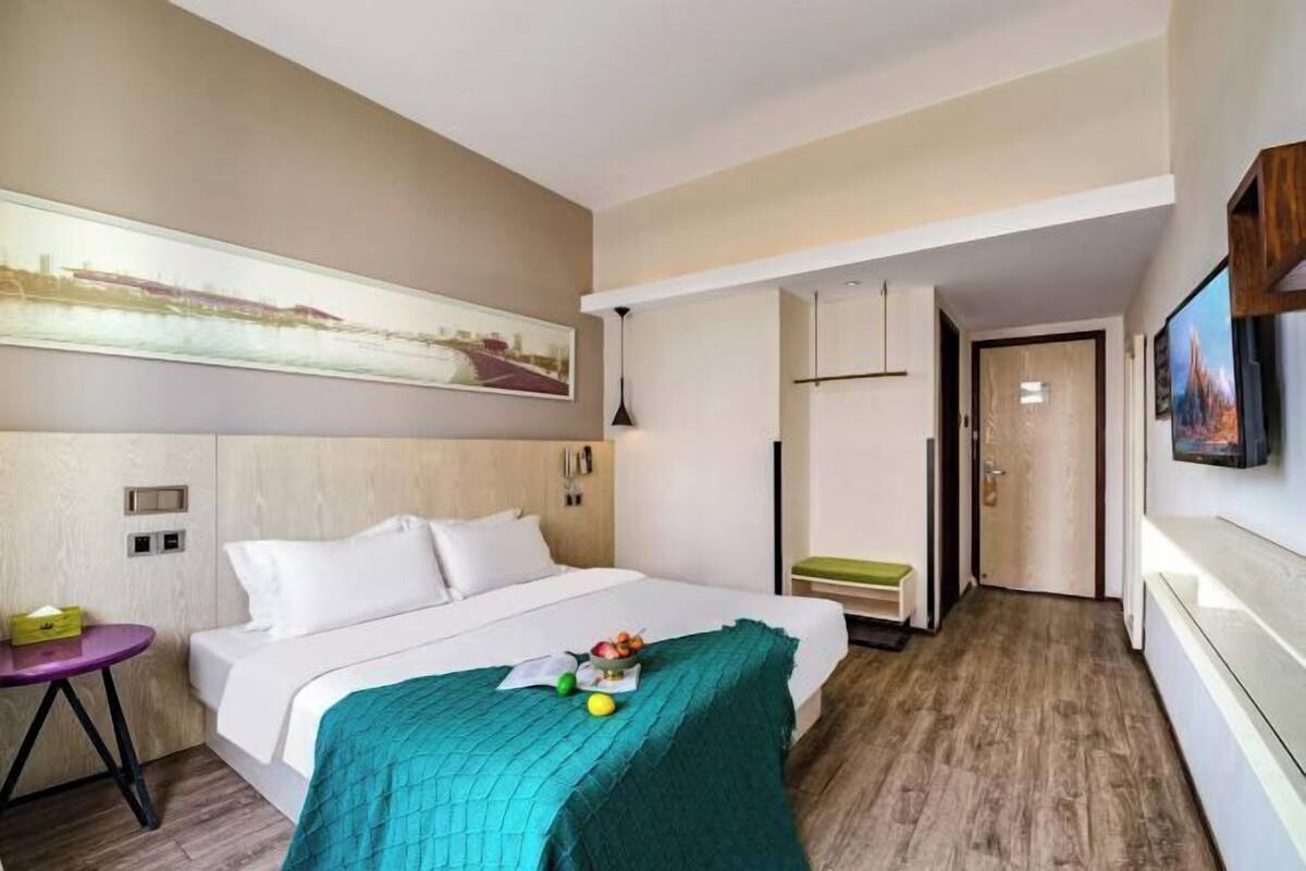 Une chambre d’hôtel avec un lit, un bureau, une chaise, un tableau au mur et une porte donnant sur une autre pièce.