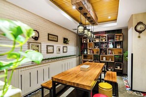 Een gezellig eetgedeelte met een houten tafel, bankjes, een boekenkast en een decoratief plafond.