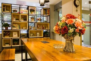 A wooden table with a vase of flowers, a smartphone, and a glass set. Behind is a bookshelf with various items. - Yayue Exquisite Hotel (Zhengzhou Erqi Square David City Branch) (Zhengzhou)