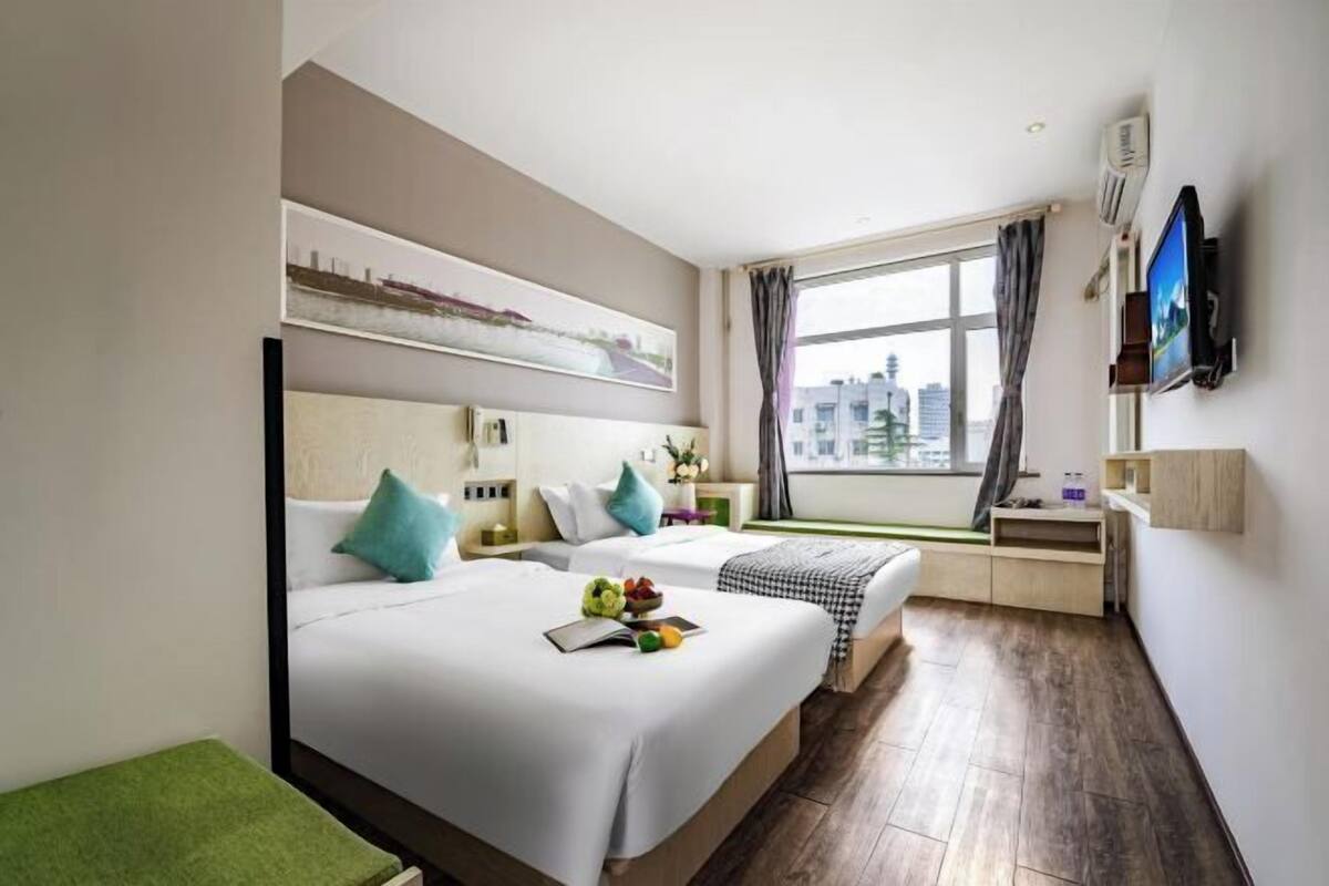 Une chambre d’hôtel avec deux lits, une télévision, une fenêtre donnant sur la ville et un bureau avec une chaise.