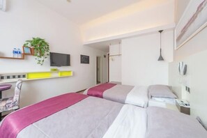 Ein Hotelzimmer mit zwei Betten, einem Schreibtisch mit Stuhl, einem Fernseher, einer Pflanze und einem Telefon an der Wand.
