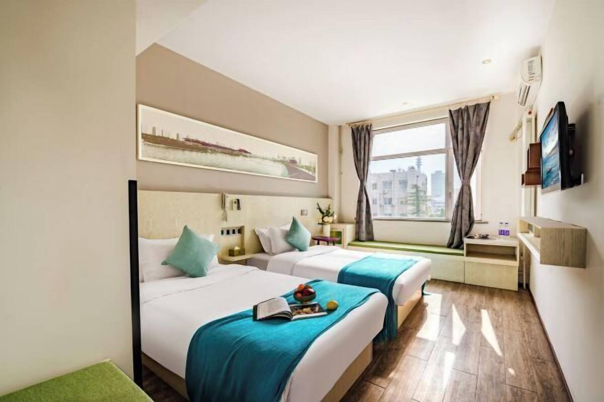 Une chambre d’hôtel avec deux lits, une grande fenêtre donnant sur la ville, un téléviseur à écran plat et un bureau avec une chaise.