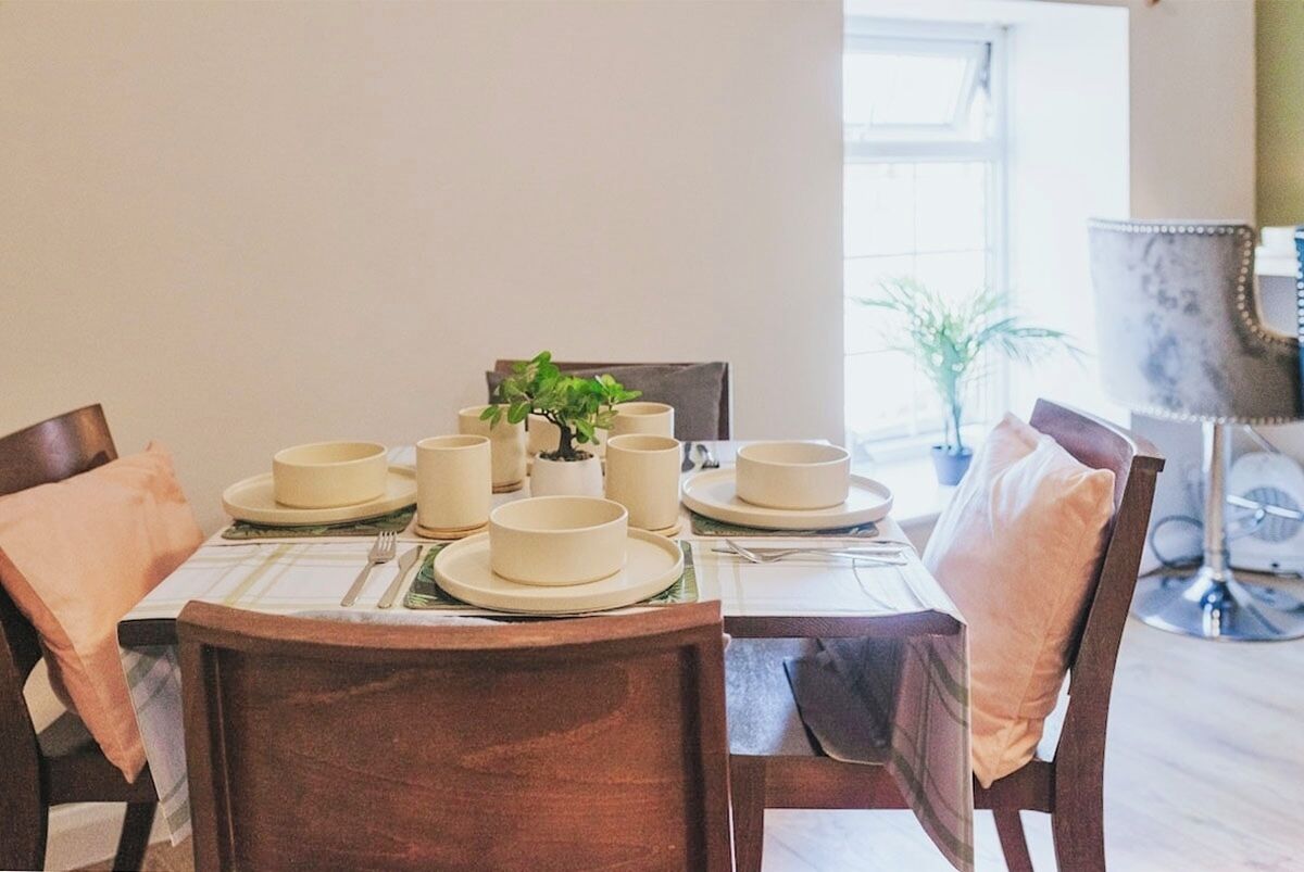 A dining table set with plates, bowls, and cups, surrounded by chairs with cushions.
