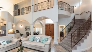Amplia sala de estar con un sofá color beige, una mesa de centro y una escalera con barandales ornamentales.