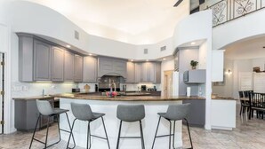 Una cocina moderna con armarios grises, una isla central con taburetes y un comedor con techo alto.