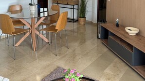 Una sala de estar moderna con una mesa de comedor de vidrio, sillas de madera, un televisor grande y un armario de madera.