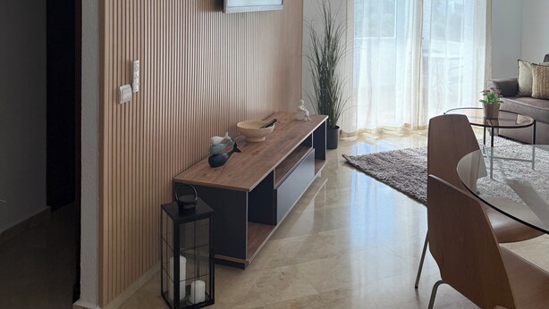 Una sala de estar moderna con un televisor de pantalla plana montado en una pared de paneles de madera, un sofá, una mesa de centro y una silla.