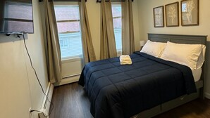 Een slaapkamer met een bed, gordijnen, een flatscreen televisie en lijstwerken aan de muur.