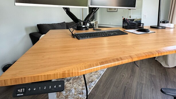 Een moderne kantoorruimte met een groot houten bureau, twee monitoren, een toetsenbord, een muis en een plafondventilator.