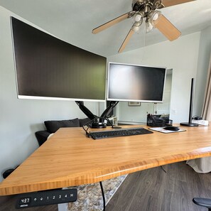 Un espacio de oficina moderno con un amplio escritorio de madera, dos monitores, un teclado, un ratón y un ventilador de techo.