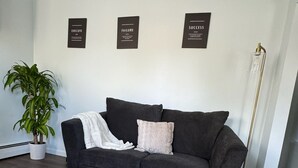 Een moderne woonkamer met een donkergrijze bank, een kamerkleed met dessin en drie decoratieve wandplaten.