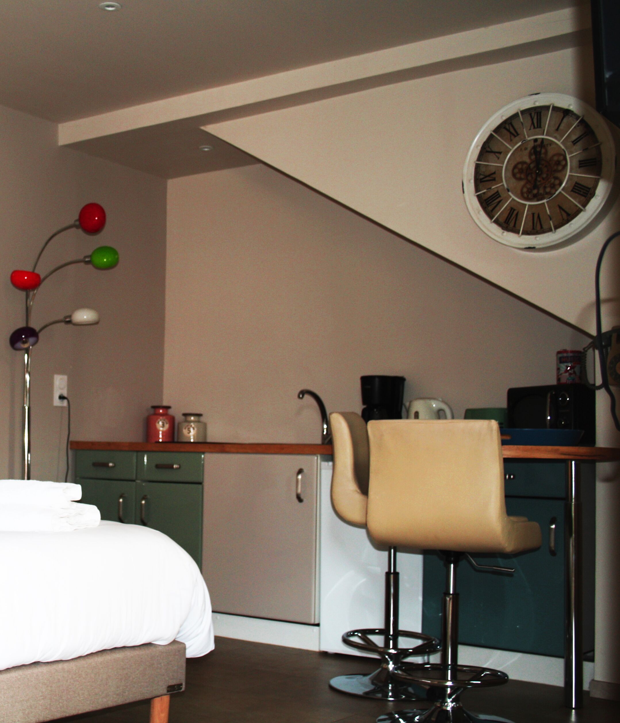 Ein Schlafzimmer mit Bett, Schreibtisch mit Stuhl, einer Uhr und einer Küchenzeile.