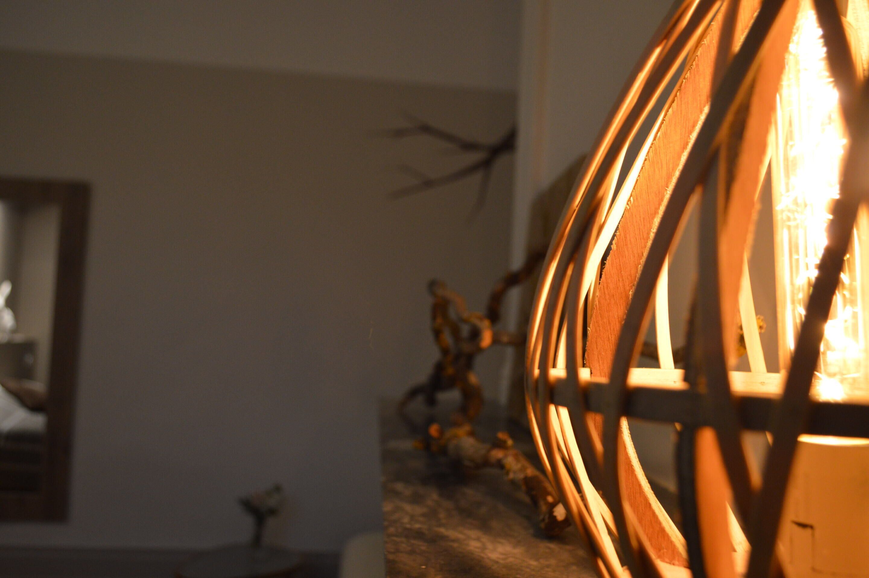 A close-up of a wooden chair with a circular backrest, a small table with a decorative item, and a wall with a branch decoration.